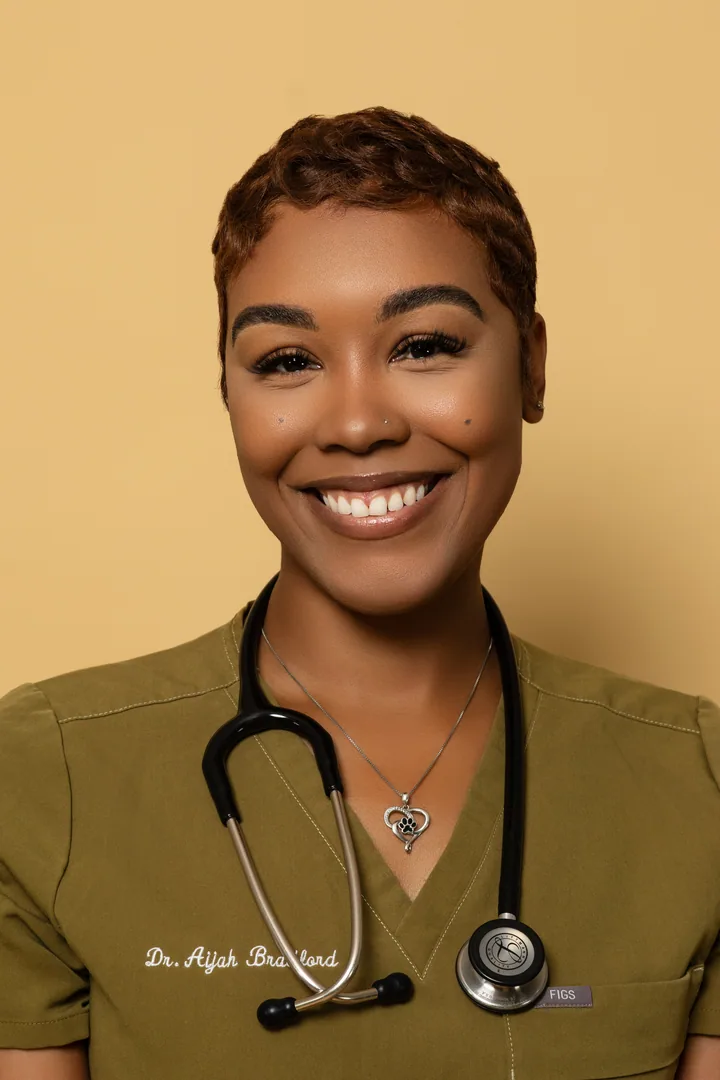 Smiling medical professional in olive scrubs against a warm gold backdrop