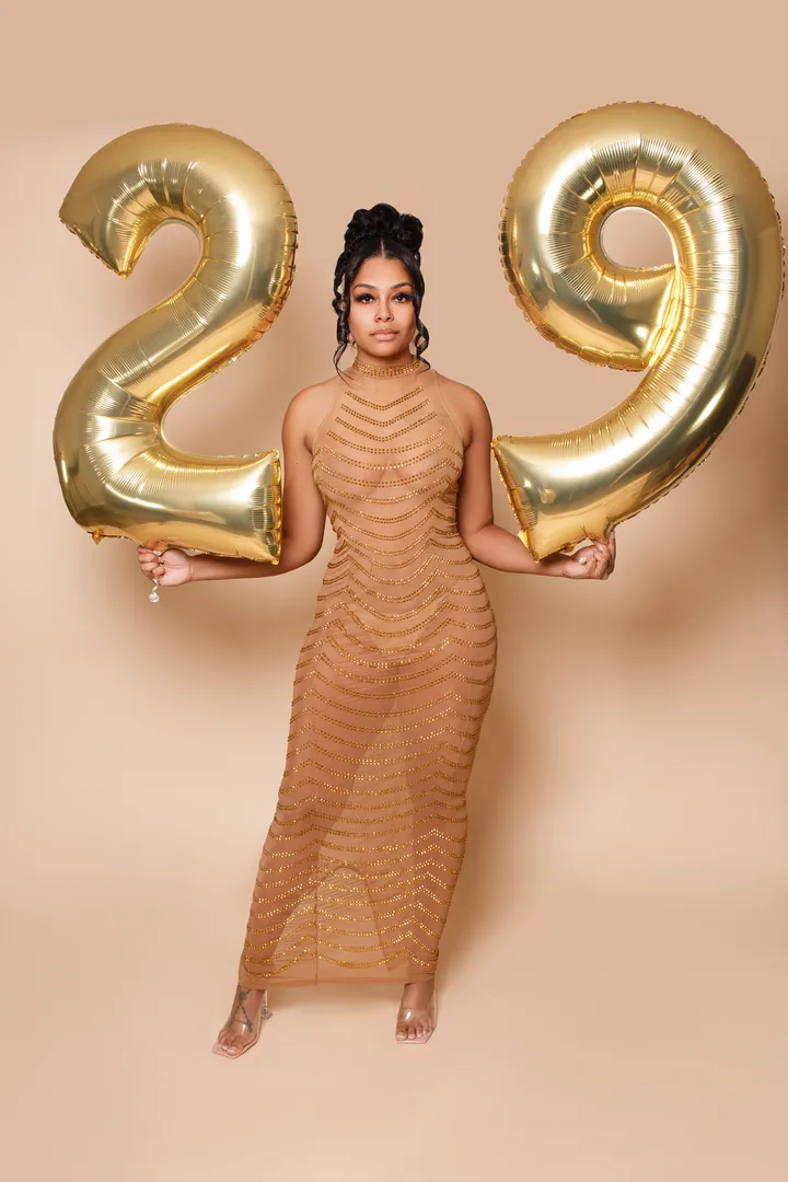 Birthday portrait with gold number balloons against a warm neutral backdrop