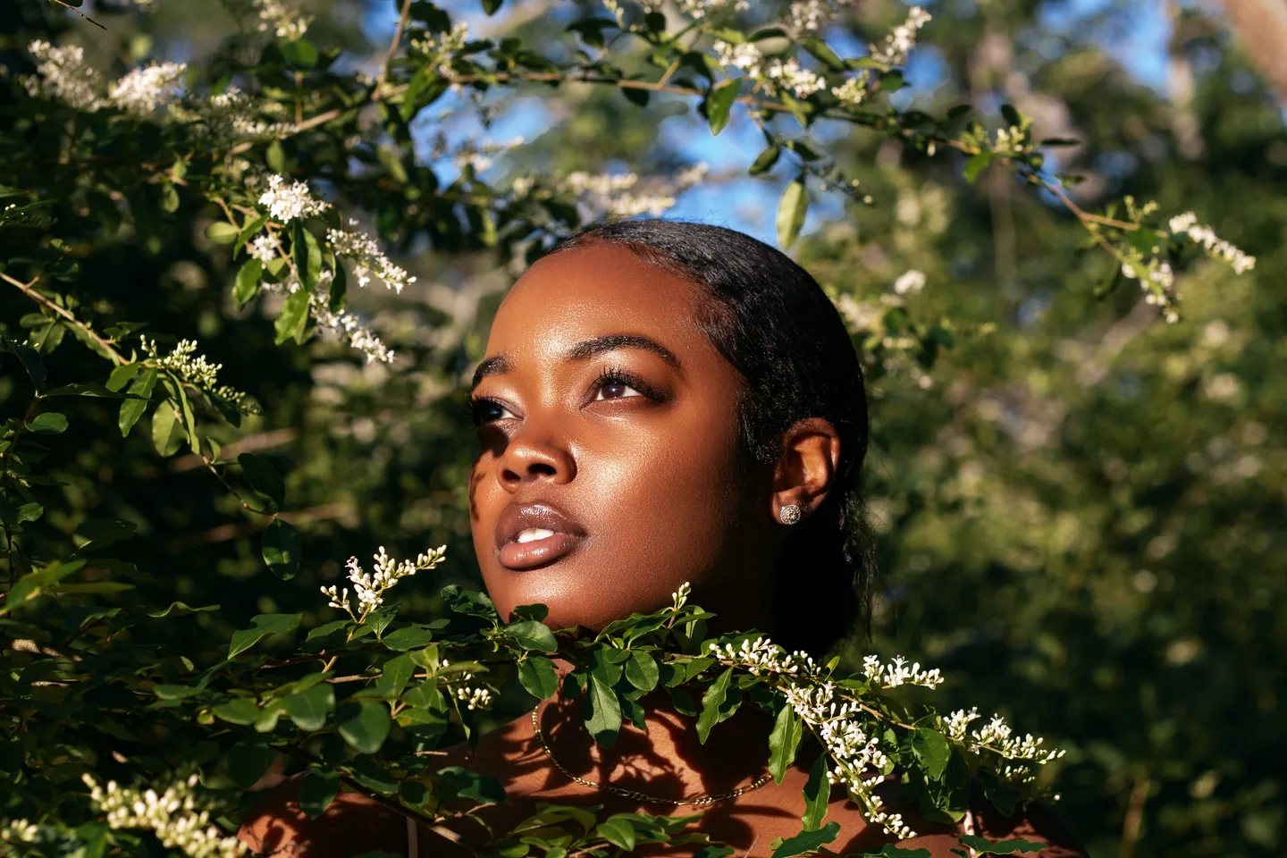 Close portrait framed by green foliage and warm sunlight